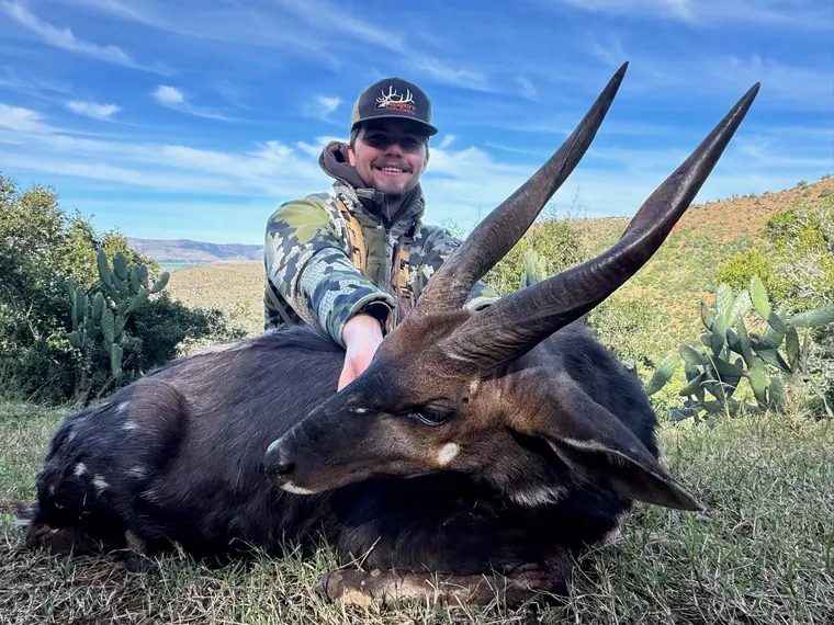 Hunter with a dark coated plains game trophy against a blue Eastern Cape sky