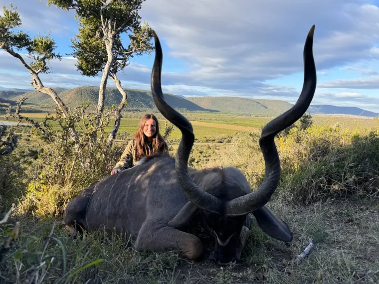 Hunter with a spiral horned trophy overlooking a green Eastern Cape valley