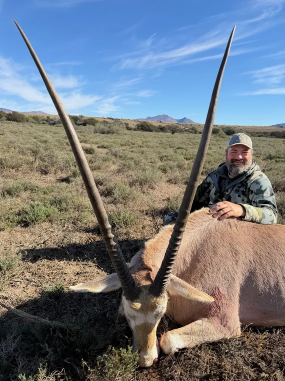 Hunter with a long horned gemsbok trophy in open South African country