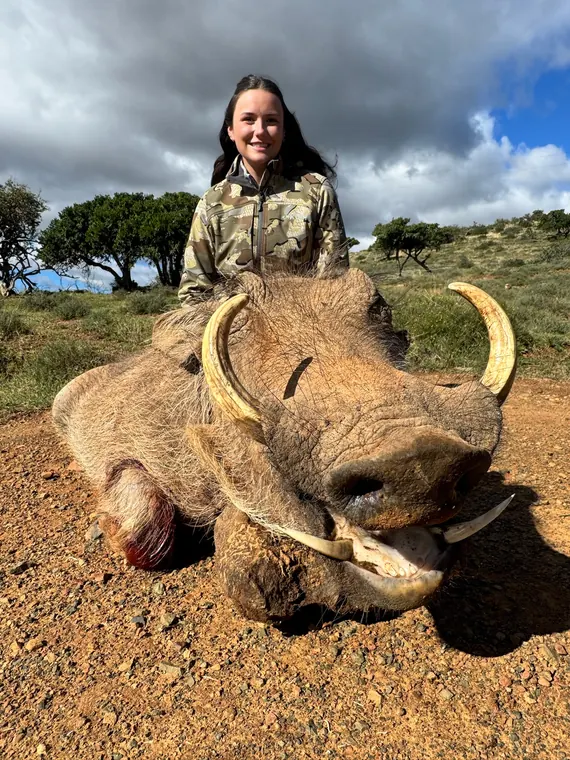Hunter with a mature warthog trophy beneath a dramatic sky