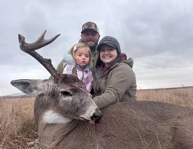 A family of three with a deer in open country