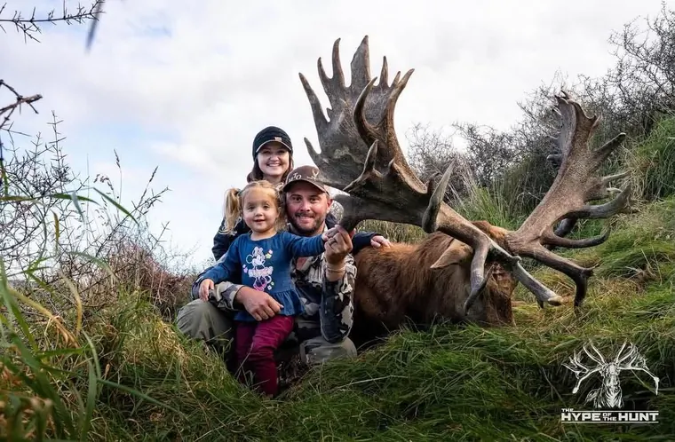A family of three with a large deer in wooded country