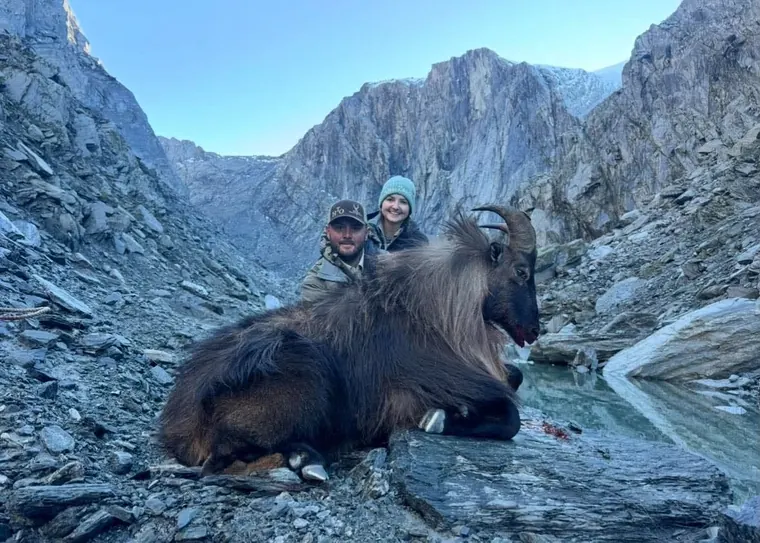 Two hunters with a hunting trophy in rocky alpine country