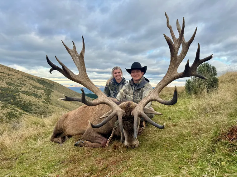 Two hunters with a mature red stag in rolling New Zealand hills