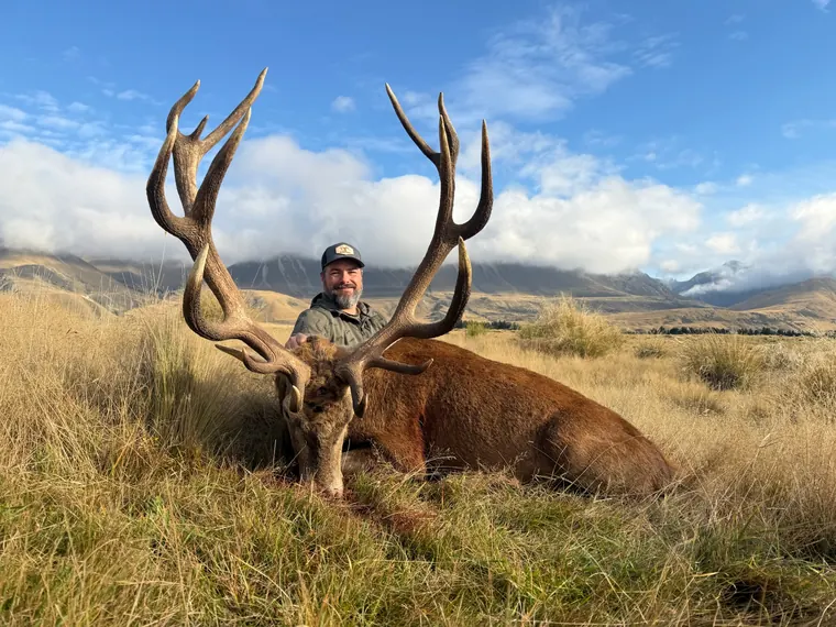 Hunter with a mature red stag beneath cloud covered New Zealand mountains