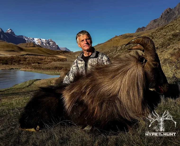 Hunter with a Himalayan tahr trophy beside an alpine lake in New Zealand