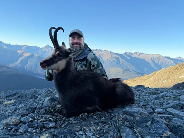 Hunter with a Himalayan tahr trophy and mountain ridges behind him
