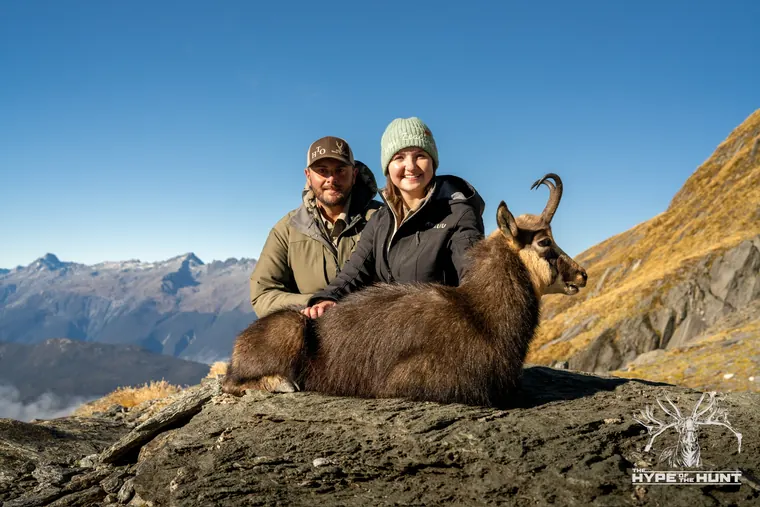 Two hunters with a Himalayan tahr on a New Zealand mountain ridge