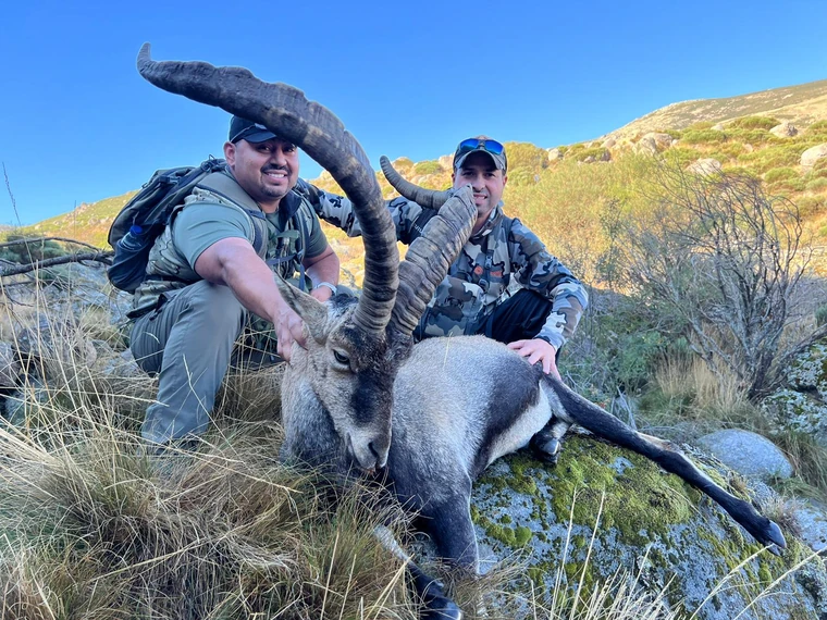 Two hunters beside a Beceite ibex in mountain scrub, Spain