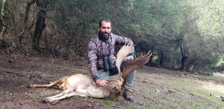 Hunter kneeling beside a fallow buck in woodland, Spain