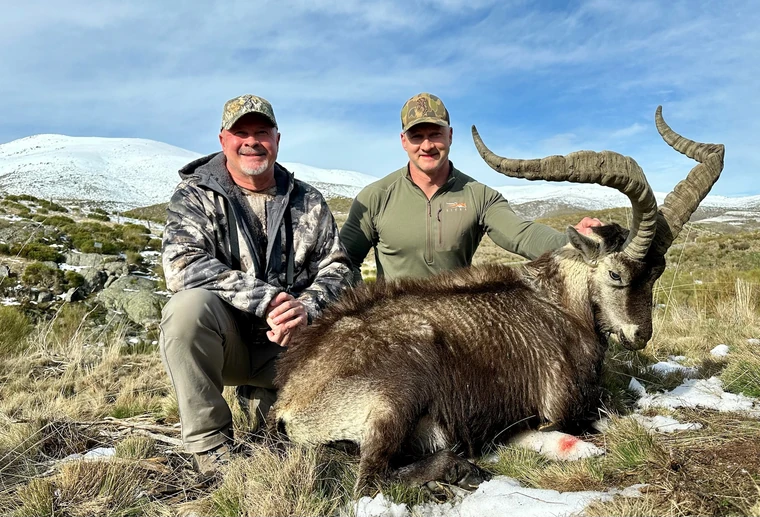 Two hunters beside a Gredos ibex with snowy hills behind them, Spain