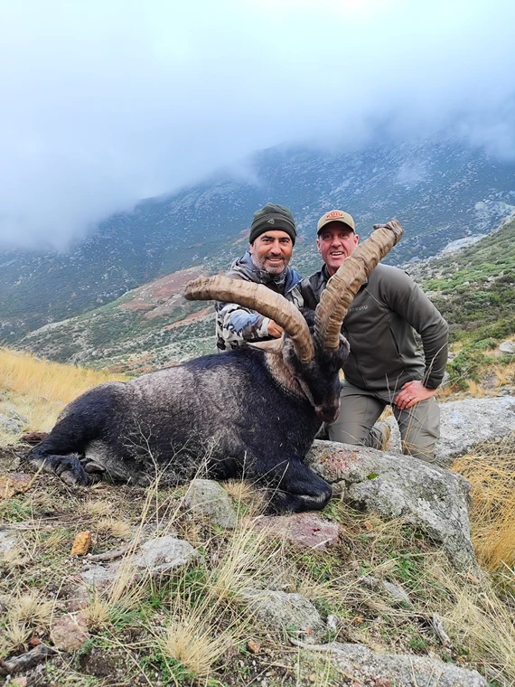 Two hunters with a Gredos ibex in cloud covered mountains, Spain
