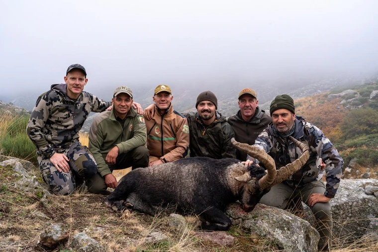 Hunting group gathered beside a Gredos ibex in the mountains, Spain