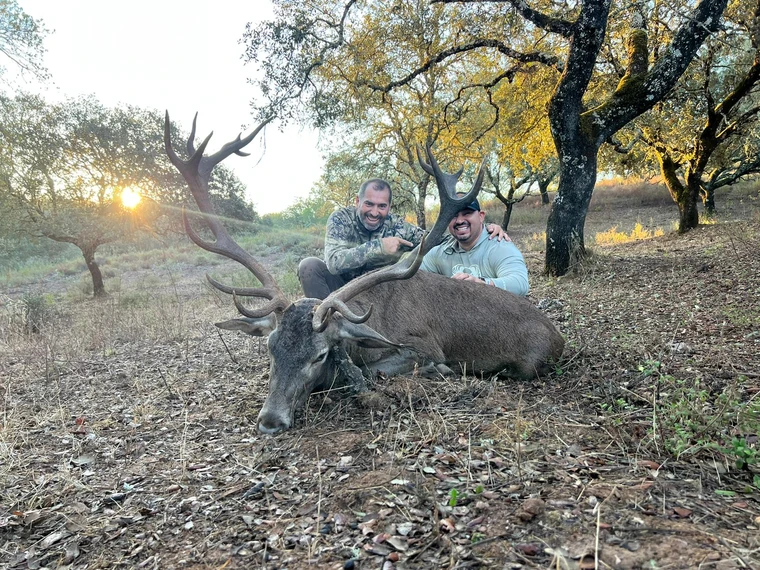 Two hunters beside an Iberian red deer beneath autumn trees, Spain