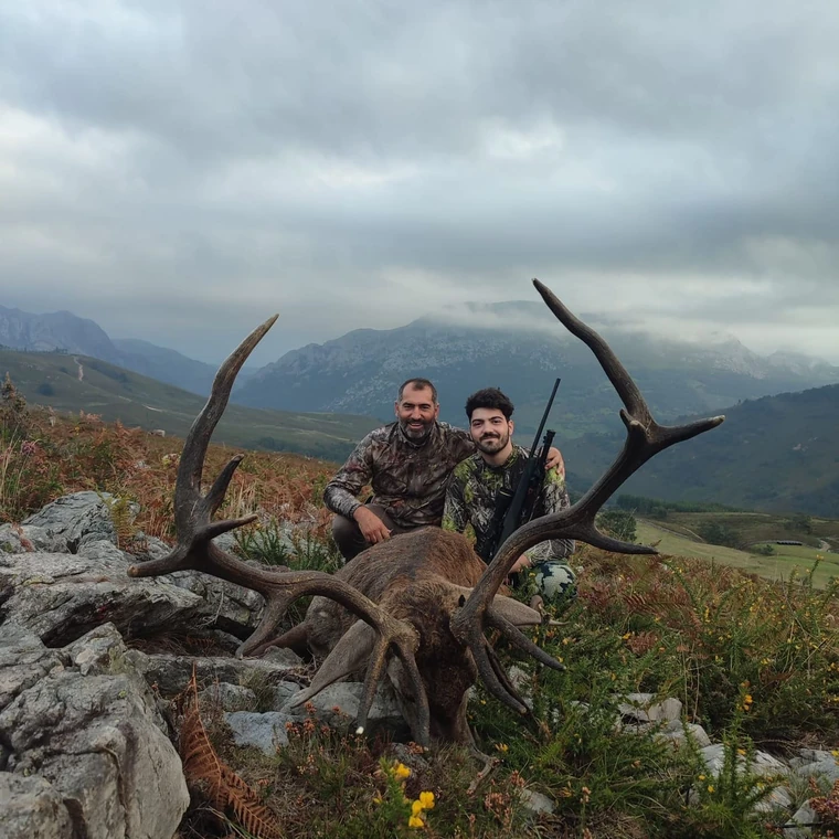 Two hunters with an Iberian red deer and hills behind them, Spain
