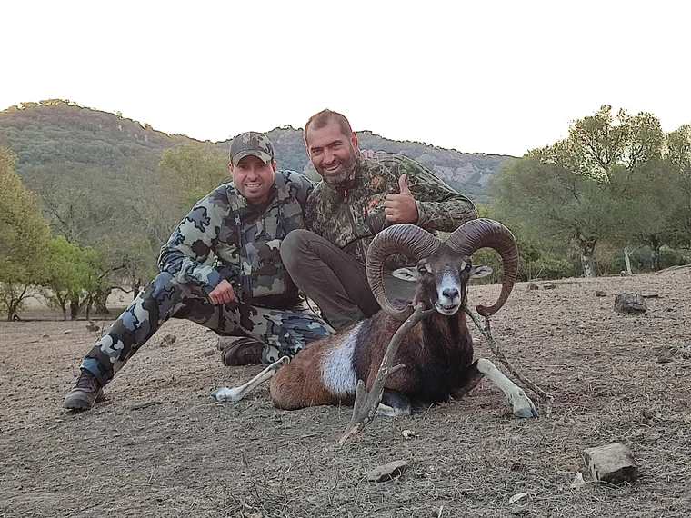 Two hunters beside a mouflon ram in rocky scrubland, Spain