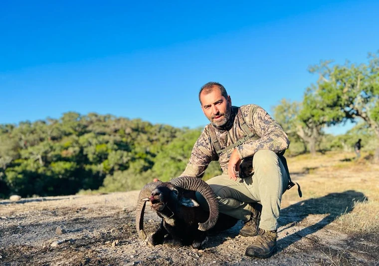 Hunter beside a mouflon ram on a sunny hillside, Spain
