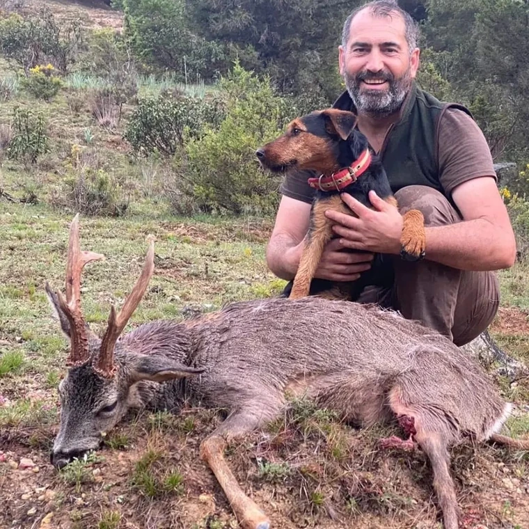 Hunter holding a dog beside a roe deer in woodland, Spain