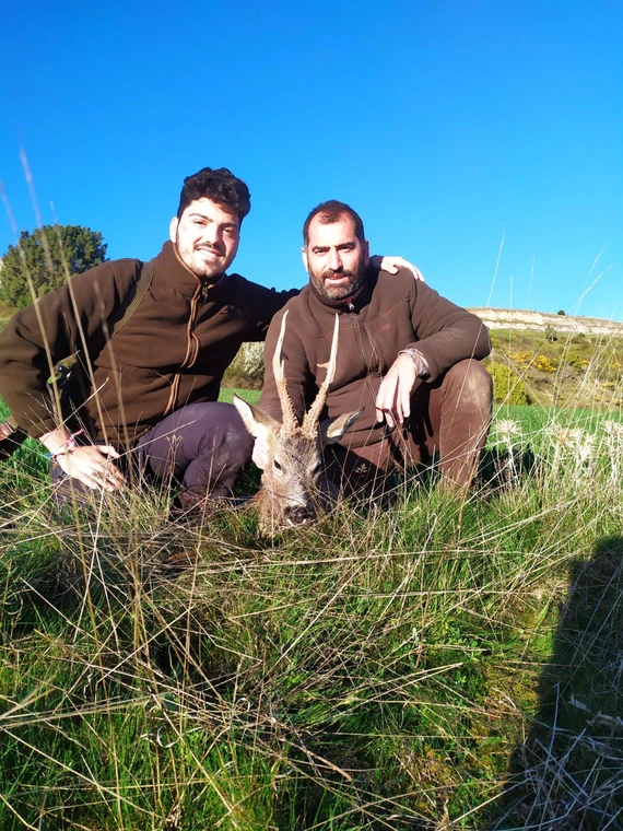 Two hunters with a roe deer on a grassy hillside, Spain