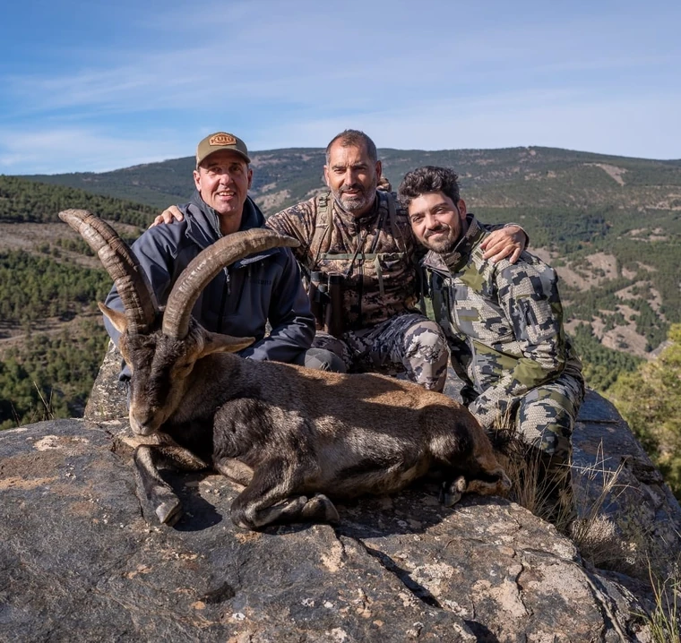 Three hunters with a Southeastern ibex in open mountain country, Spain
