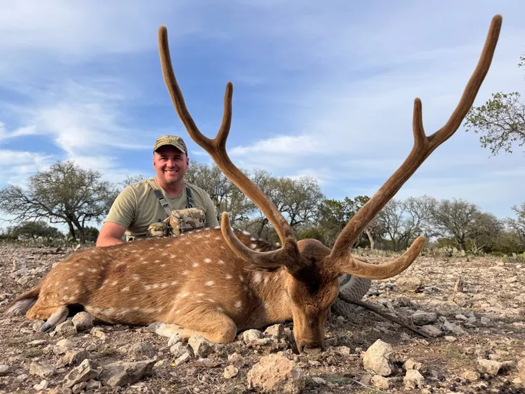 Hunter with a mature axis buck in rocky Texas terrain