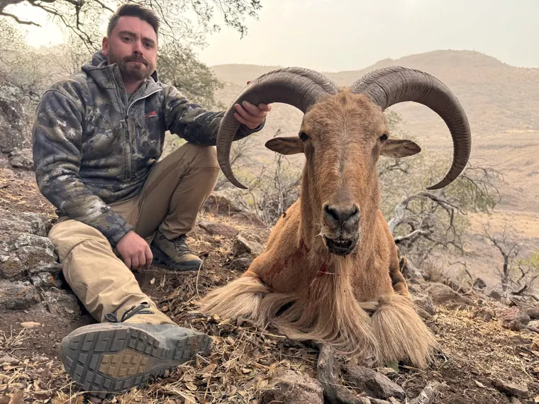Hunter and aoudad ram with rugged West Texas mountains behind them